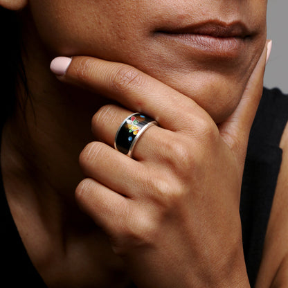 Close-up of a person wearing a ring with a colorful design on a neutral background